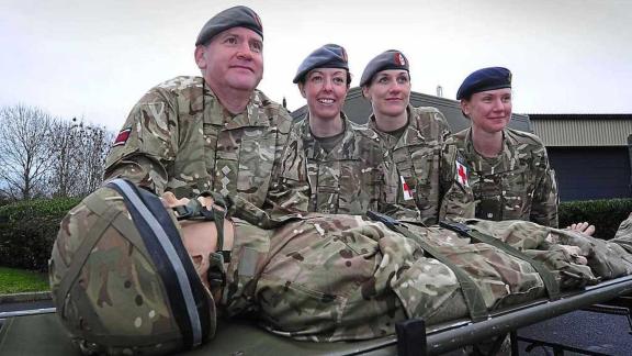 Four people posing in front of a medical training dummy on a stretcher, all representing themselves as United Kingdoms Army Reservists.