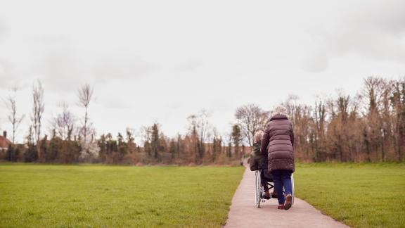 A carer pushing a person in a wheelchair up a path and into the distance.