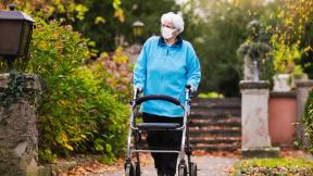 An elderly woman walking through hospital grounds with the aid of a stroller.