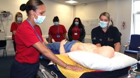 A group of student gathered around a bed taking part in a training exercise.