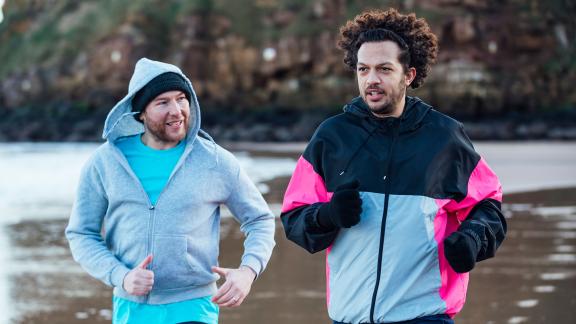 Two men jogging on a beach.