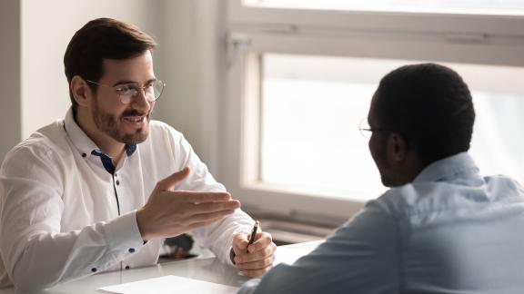 Two office workers having a conversation across a desk.