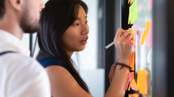 An office worker writing on a post-it note attached to a wall.