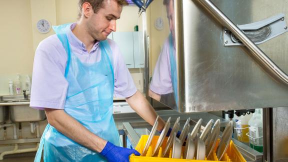 An apprentice dishwasher using an industrial dishwasher.