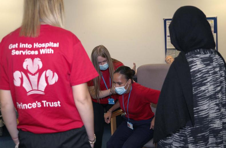 A group of young people learning to help a patient out of a chair.